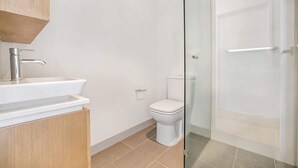 A modern bathroom with a white sink, toilet, and glass shower enclosure. - Comfy 2-Bed Balcony Unit near Iconic Chapel St (Prahran)