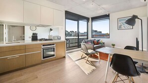 A modern kitchen with a dining area, large windows, and a view of the city. - Comfy 2-Bed Balcony Unit near Iconic Chapel St (Prahran)
