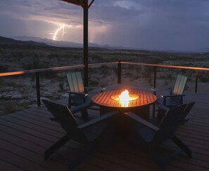 A deck with a round table and chairs, a fire pit, and a view of a desert landscape with mountains in the background. - Big Bend StarGazer:Retro Airstream,Neolithic Views (Terlingua)
