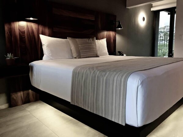 Une chambre à coucher moderne avec un grand lit, une tête de lit en bois foncé et une vue sur l’extérieur.