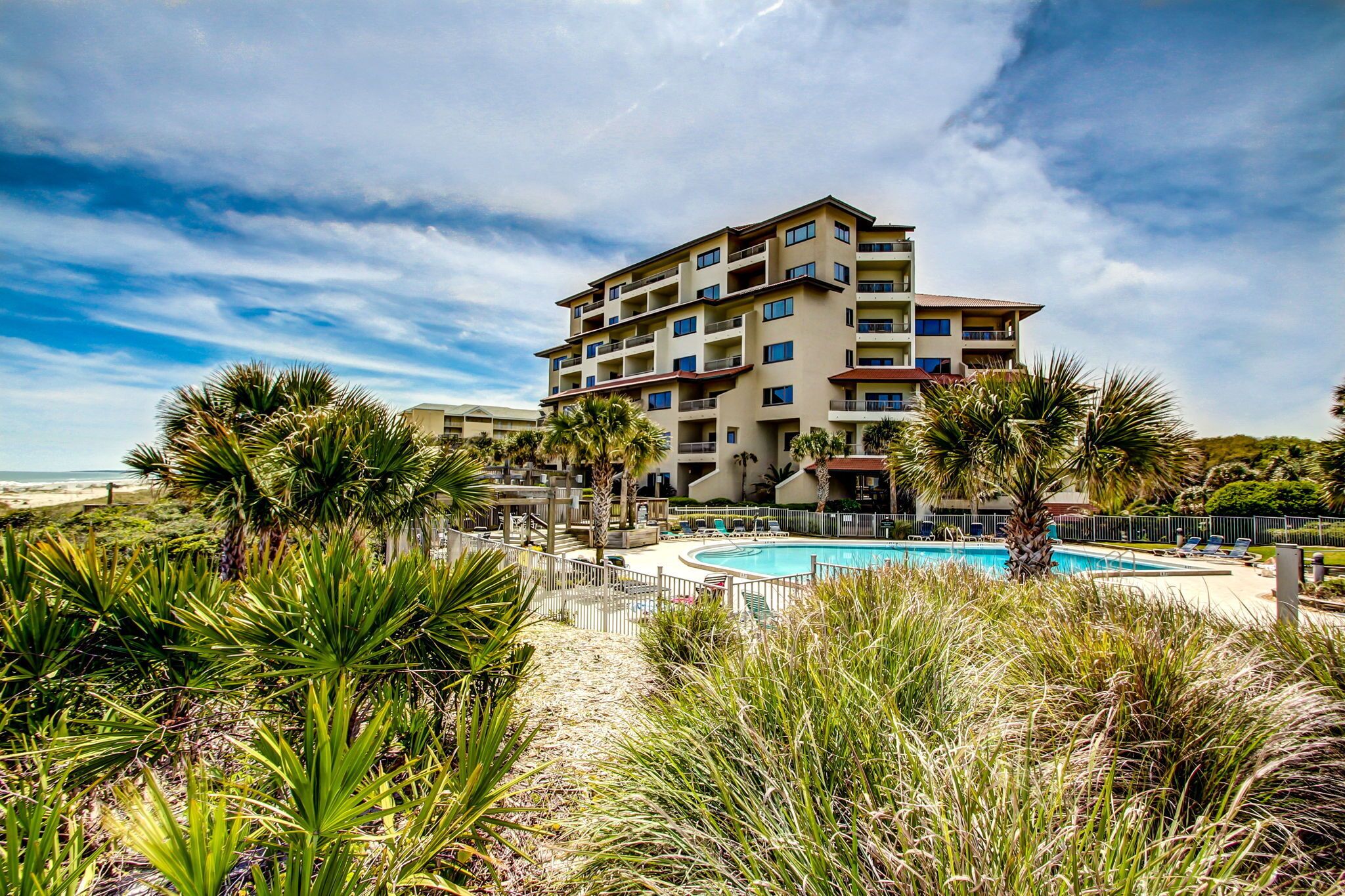 Ein mehrstöckiges Hotel mit Swimmingpool, umgeben von tropischer Vegetation und Blick auf einen Strand.