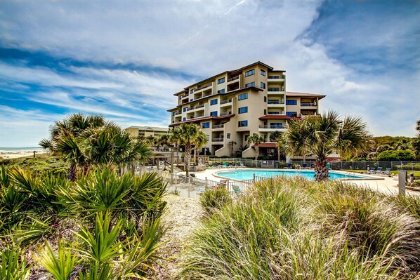 Un hotel de varios pisos con piscina, rodeado de plantas tropicales y vistas a la playa.