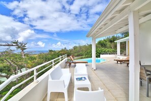 Un espace extérieur abrité avec une piscine, des chaises longues blanches et une vue sur l’océan.