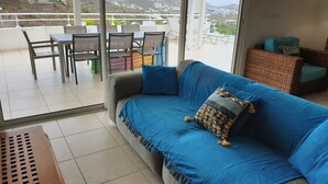 A balcony with a blue sofa, a dining table with chairs, and a view of mountains and houses. - Villa JELUCA Beautiful and spacious villa with swimming pool (SAINT MARTIN)