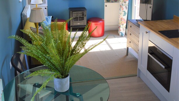 A kitchen with a glass table, a red stool, and a potted plant. - Cockloft, Romantic Countryside Hideaway (Bishops Cannings)