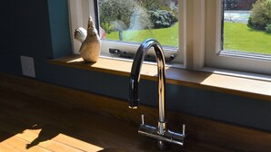 A kitchen with a stainless steel sink, a window with a view of a garden, and a shelf with a ceramic pot. - Cockloft, Romantic Countryside Hideaway (Bishops Cannings)
