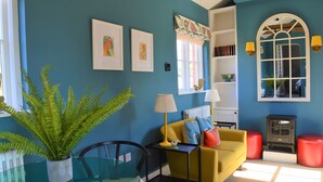 A room with a blue wall, a yellow sofa, a glass table, and a red radiator. - Cockloft, Romantic Countryside Hideaway (Bishops Cannings)