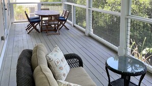A covered porch with a wooden table and chairs, a cushioned sofa, and a glass-top table.