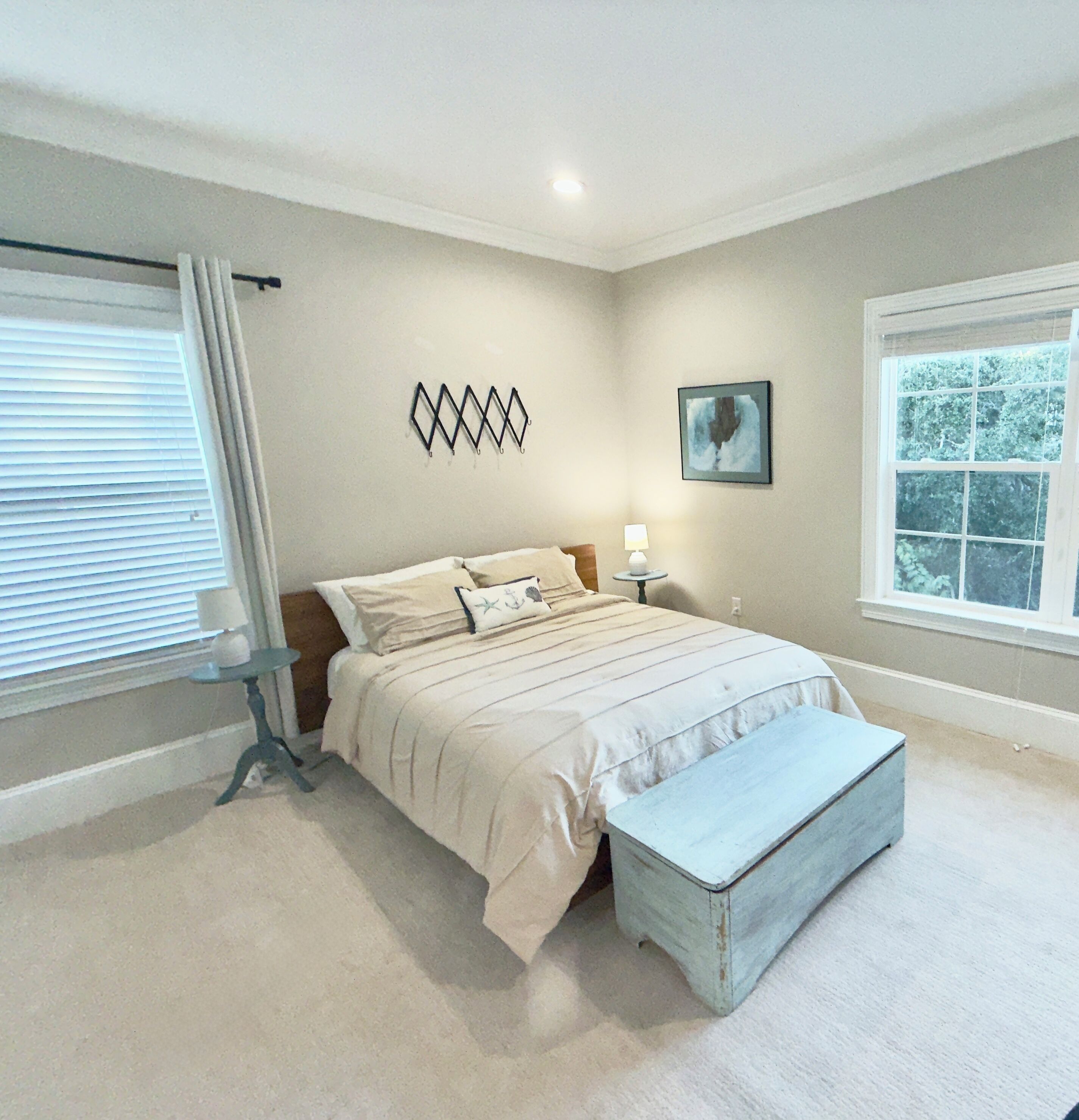A bedroom with a bed, bedside table, lamp, artwork, and a window.