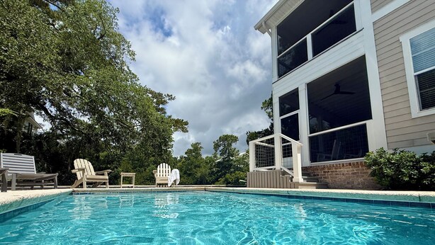 A swimming pool with clear water, surrounded by a deck with lounge chairs and a covered area.
