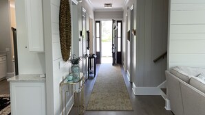 A hallway with white walls, a beige rug, and a grey sofa.