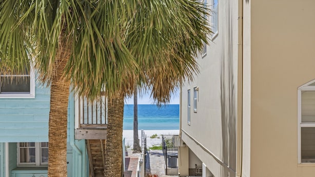 A coastal building with a balcony overlooking the beach, a staircase leading to the entrance, and a clear view of the ocean.