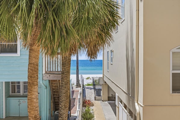 A coastal building with a balcony overlooking the beach, a staircase leading to the entrance, and a clear view of the ocean.