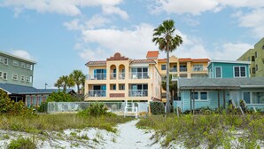 A beachfront property with a sandy path leading to a multi-story building with balconies.