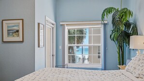 A bedroom with a bed, a window with a view, a potted plant, and a framed picture on the wall.