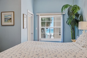 A bedroom with a bed, a window with a view, a potted plant, and a framed picture on the wall.