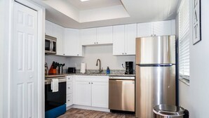 A compact kitchen with white cabinets, stainless steel appliances, and a skylight. - New Modern Chic Suite Walkable Steps to Beach (Indian Rocks Beach)