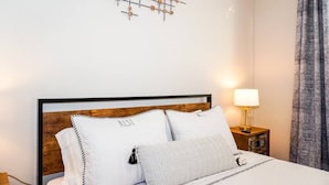 A neatly made bed with white bedding and striped pillows, a wooden headboard, and a wall-mounted decorative piece. - New Modern Chic Suite Walkable Steps to Beach (Indian Rocks Beach)