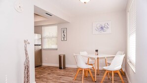 A dining area with a white table and chairs, a clock, and a framed artwork on the wall. - New Modern Chic Suite Walkable Steps to Beach (Indian Rocks Beach)