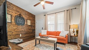 A cozy living room with a wooden wall, a sofa, a coffee table, a TV, and a lamp.