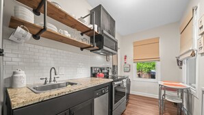 A modern kitchen with a granite countertop, stainless steel appliances, and wooden shelves.