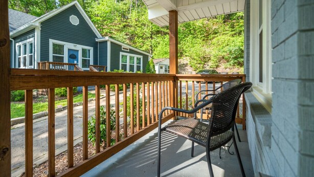 A porch with a wooden railing, a black wicker chair, and a view of a house with a blue door and a garage.