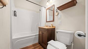 A bathroom with a bathtub, toilet, vanity, and a mirror.