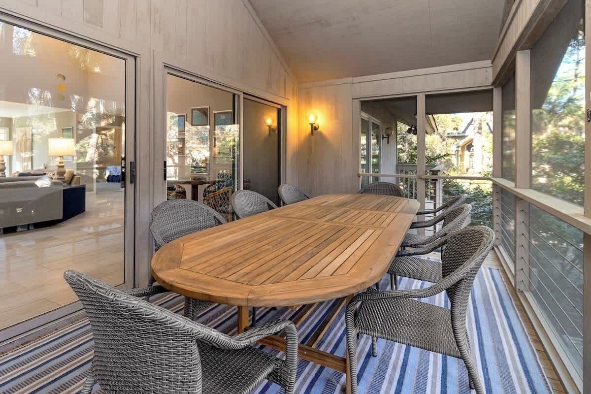 Un'area pranzo moderna con tavolo in legno e sedie in vimini, ampie finestre e vista sull'interno.