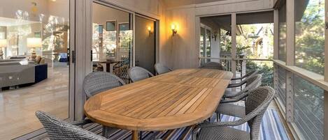 Un'area pranzo moderna con tavolo in legno e sedie in vimini, ampie finestre e vista sull'interno.