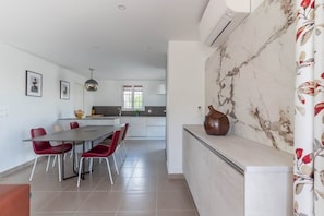 Eine moderne Küche mit Marmor-Spritzschutz, einem Essbereich mit roten Stühlen und einer großen Vase auf der Arbeitsplatte.