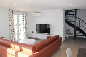 A modern living room with a sofa, a TV, a staircase, and a chair.