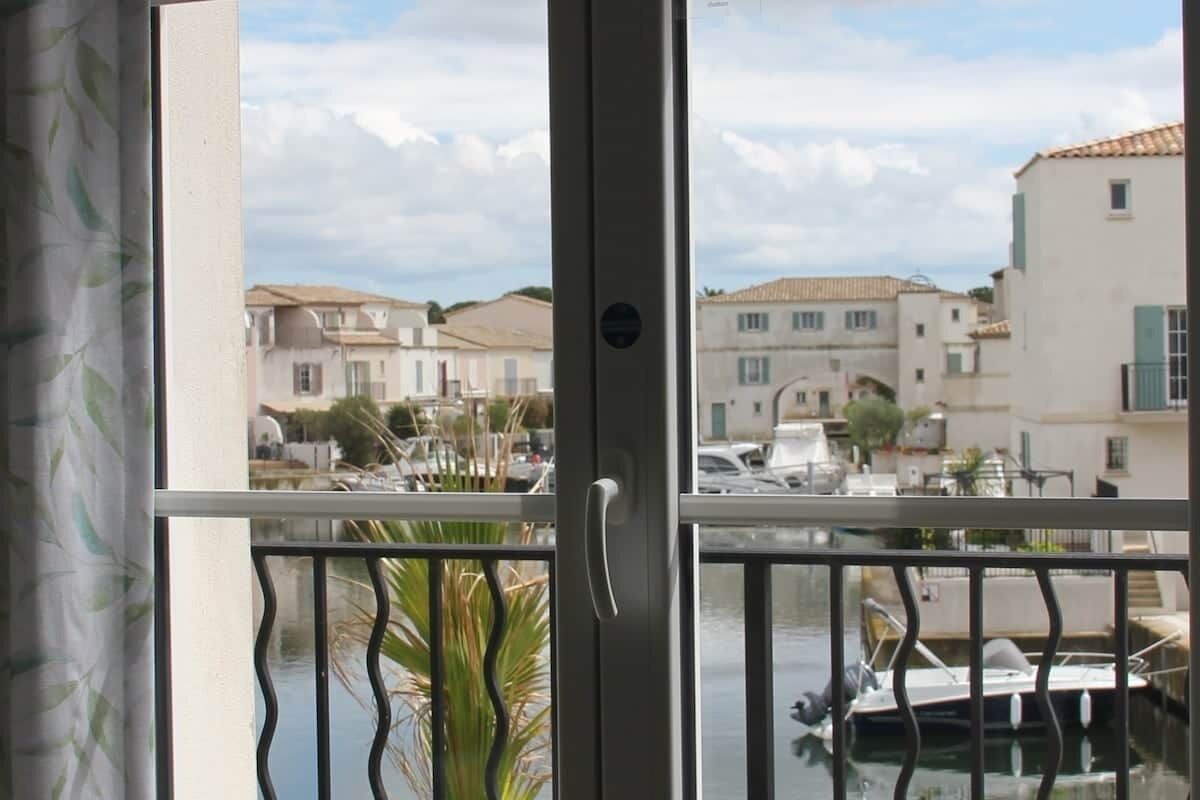 A view through a window with a balcony railing, a door, and a view of a marina with boats and buildings.
