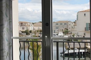 A view through a window with a balcony railing, a door, and a view of a marina with boats and buildings.