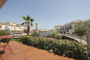 Eine Holzterrasse mit einem roten Klappstuhl, einer Palme und Blick auf Gebäude im Hintergrund.