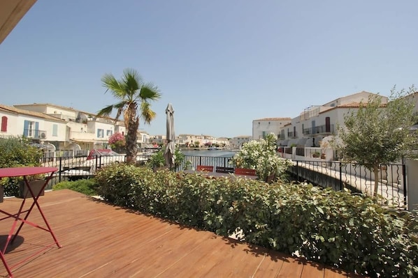 A wooden deck with a red folding chair, a palm tree, and a view of buildings in the background.