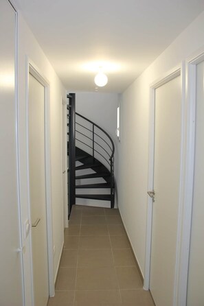 A narrow hallway with a spiral staircase, white doors, and a light fixture on the ceiling.