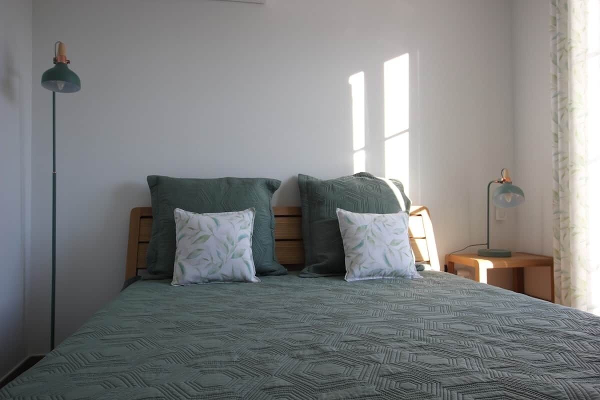 Un lit avec une couvre-lit à motifs, deux oreillers, une table de chevet, une lampe et une fenêtre avec des rideaux.