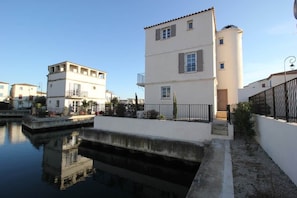 A canal-side building with a white facade, a small balcony, and a staircase leading to the entrance.