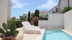 Un área junto a la piscina con sillones de descanso, una planta en maceta y una piscina azul cristalina.