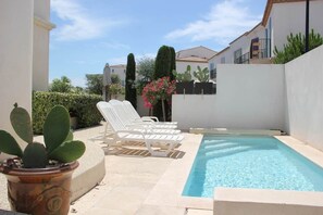 Un área junto a la piscina con sillones de descanso, una planta en maceta y una piscina azul cristalina.