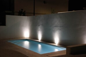 A swimming pool with a lighted wall, a concrete floor, and a dark surrounding area.