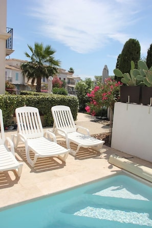 A pool area with white lounge chairs and a clear blue pool.