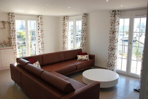 A modern living room with a brown sofa, a round coffee table, and large windows with floral curtains.