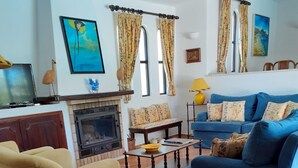 Ein Wohnzimmer mit einem beigefarbenen Sessel, einem blauen Sofa, einem Kamin und einem Fliesenboden.