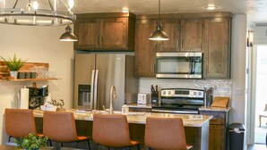 Une cuisine compacte dotée de meubles en bois, d’appareils électroménagers en acier inoxydable et d’un îlot central avec des tabourets de bar.