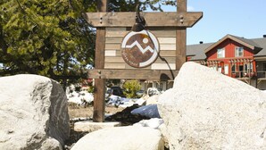Un panneau en bois orné d’un symbole représentant la randonnée, indiquant un sentier ou un chemin.