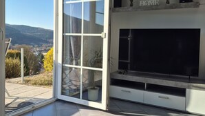 Un salon moderne avec un grand téléviseur, des portes-fenêtres coulissantes donnant sur une terrasse et un panneau décoratif portant l’inscription « HOME » sur le mur.
