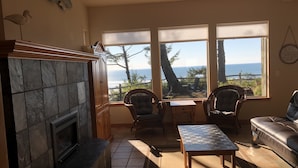 Ein gemütliches Wohnzimmer mit Kamin, bequemen Sitzgelegenheiten und großen Fenstern mit Blick auf den Ozean.