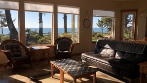 Ein Wohnzimmer mit Meerblick, eine Ledersofa, zwei Korbstühle und ein kleiner Tisch.