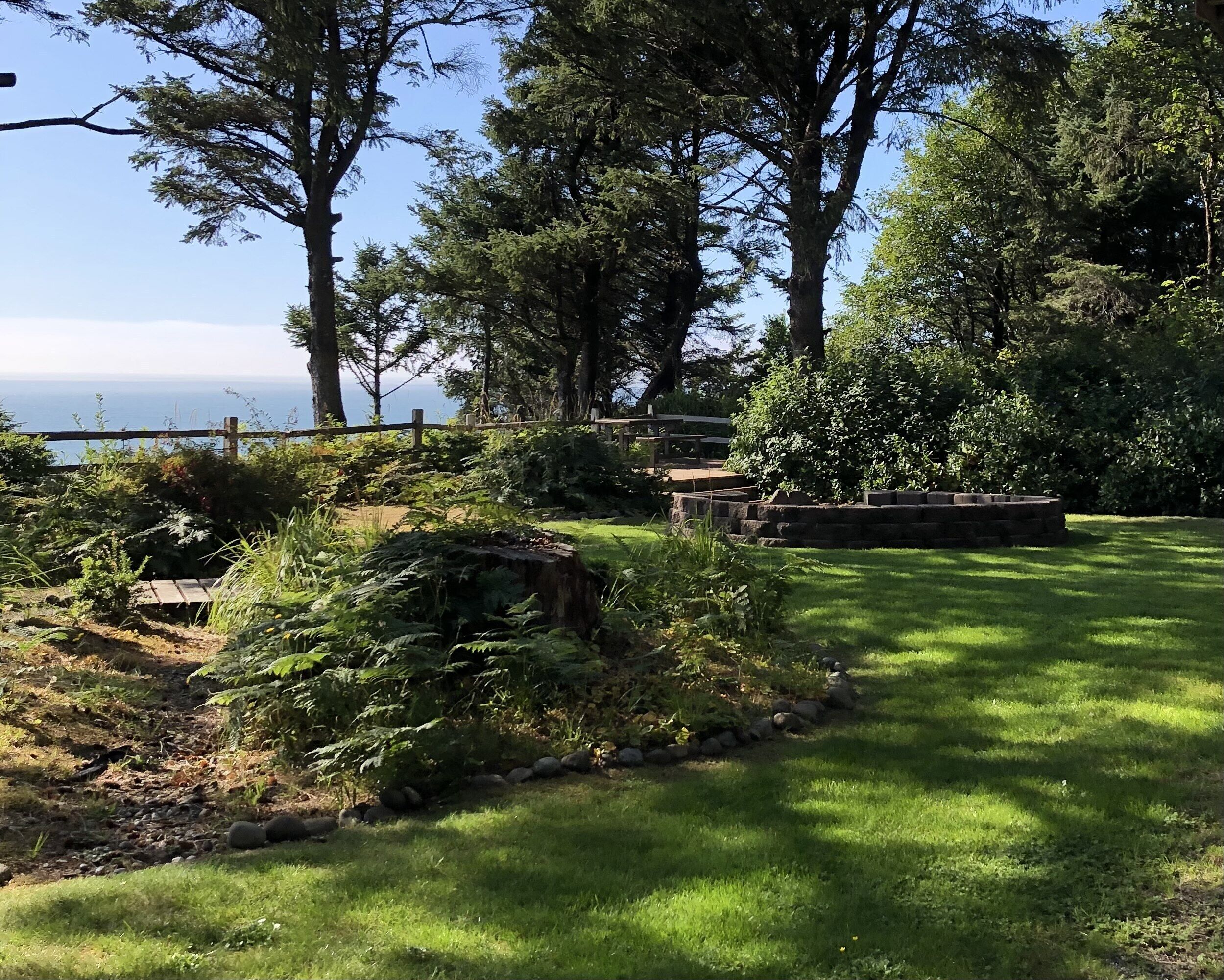 Un jardin luxuriant avec un banc en pierre, une clôture en bois et une vue sur la mer.